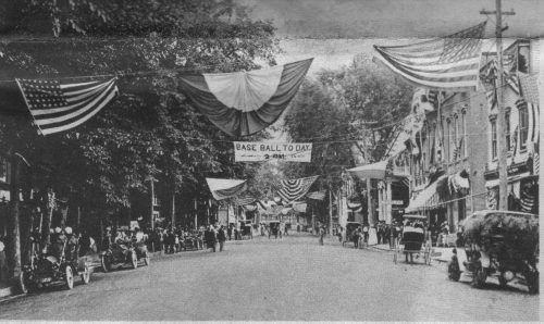 Main Street 1912 with flags hanging and a sign reading "Base Ball Today 9am."