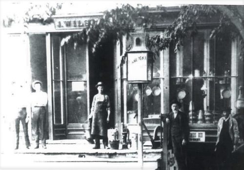 Black and white photograph showing five people near the lamp and a tin shop.