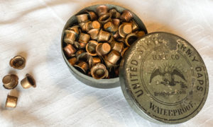 Percussion cap container partly open showing caps inside. The lid contains the words "United States Army Caps Waterproof."