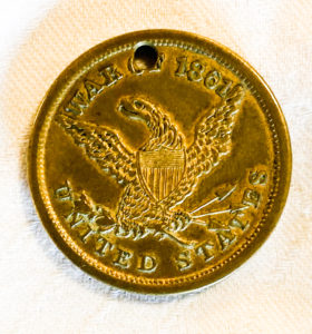 One side of Captain Clark's identity disc. It has an engraving of an eagle with a shield representing the American Flag on its chest. Above it are the words "War" and "1861." Below the eagle is the name "United States."