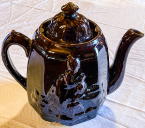 Dark teapot with engraving of woman by a well.