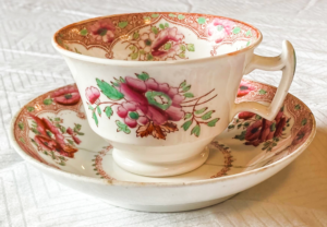 Tea cup in a bowl with flowers painted on both.