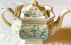 White Octagon shaped tea pot with an illustration of houses by the water engraved.