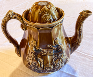 Brown teapot with engraving of people sitting at a table.