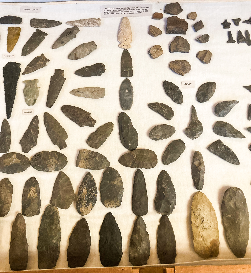 This photograph contains a sign that reads "This collection of Indian Relics was gathered and owned by Arthur U. Stevenson of Middleburgh, Schoharie County Historian. Nearly all of these relics were found in the Schoharie Valley.