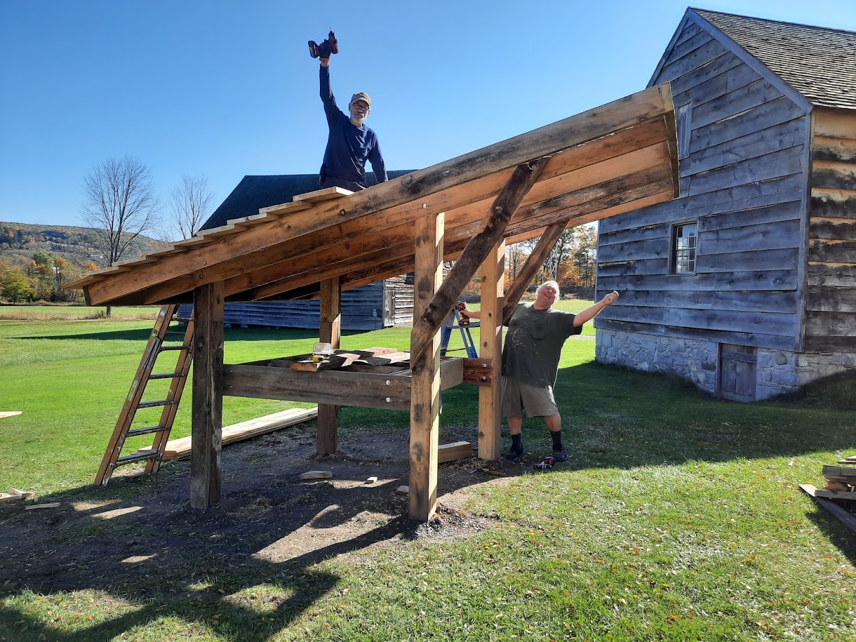 Two men building roof for bee hive oven.