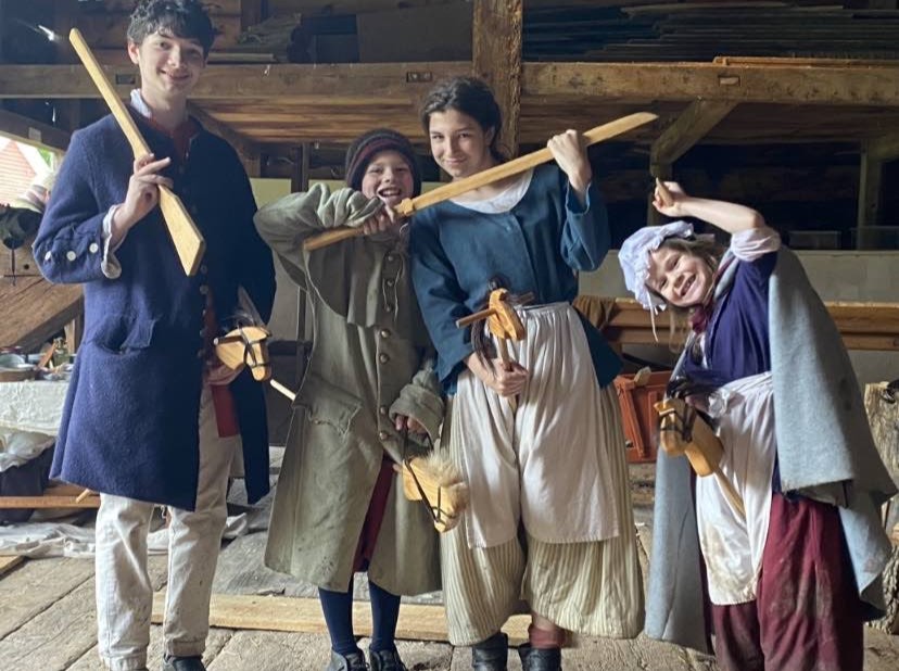 Kids dressed in colonial attire playing with 18th century toys.