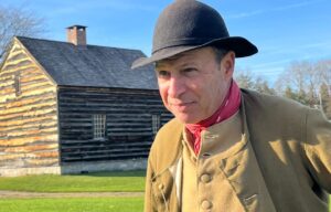 18th Century living historian with Hartmann's Dorf house in background.